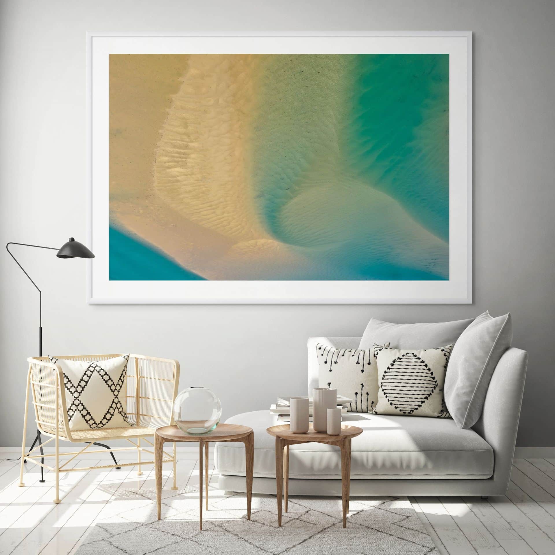 A modern living room with a white sofa, rattan chair, round wooden tables, and "CONFLUENCE" limited edition fine art in beige and teal with museum-grade framing displayed above on the grey wall. - The Coastal Edit Australia